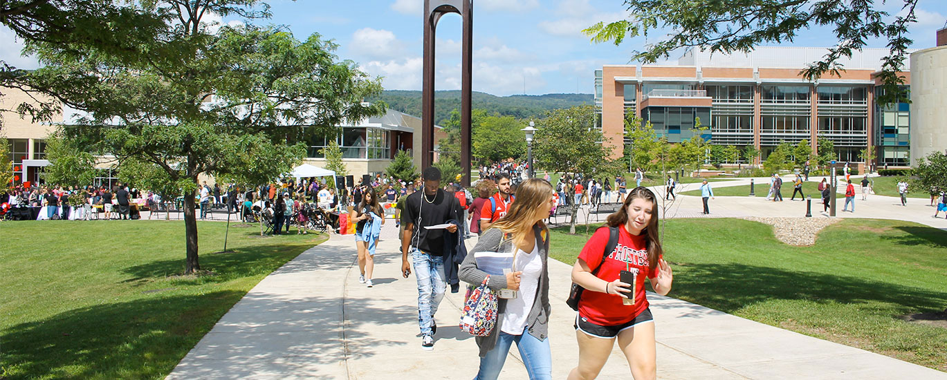 A large group of Frostburg State students walk to class near the campus clocktower on a warm, sunny day